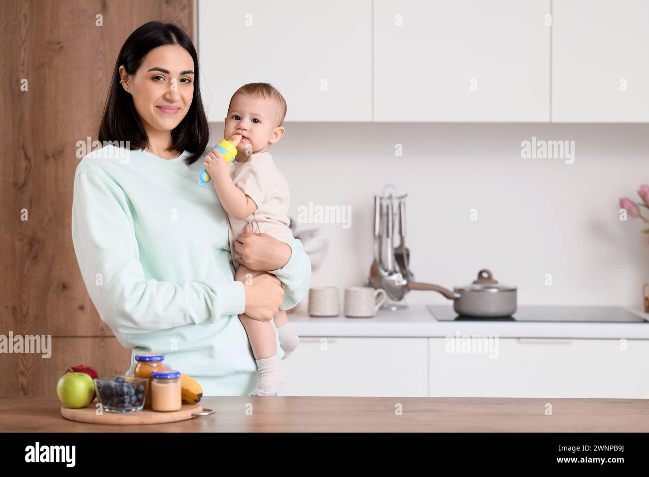 Mother giving her little baby nibbler with food in kitchen Stock Photo