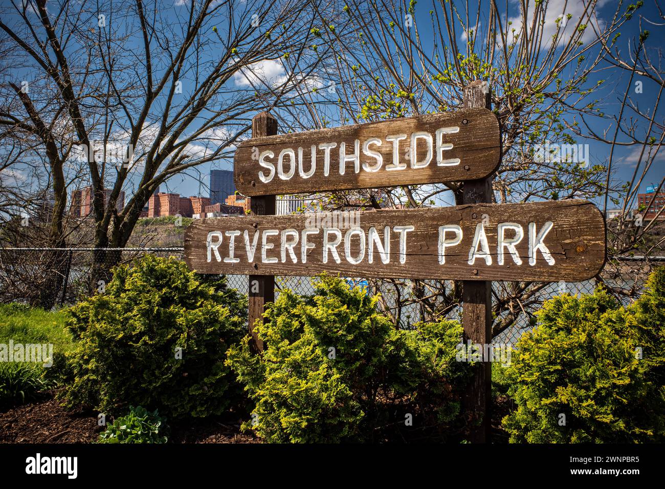 On a picturesque spring day, the South Side Riverfront Park sign stands proudly against the backdrop of downtown Pittsburgh, under a serene, clear blu Stock Photo