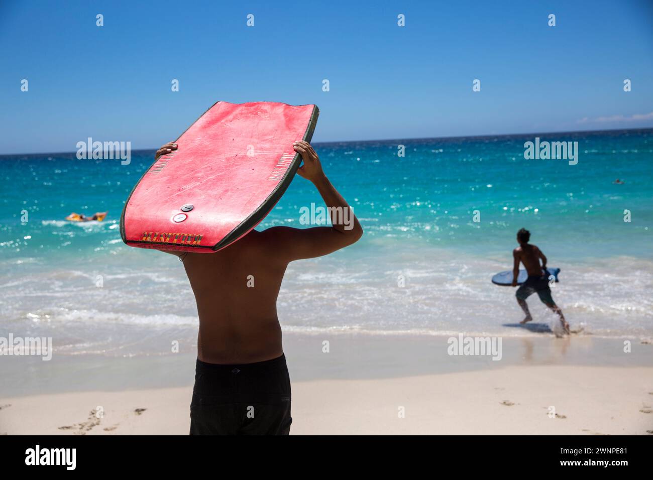Locals ride the waves on a white sand beach on Hawaii. Stock Photo