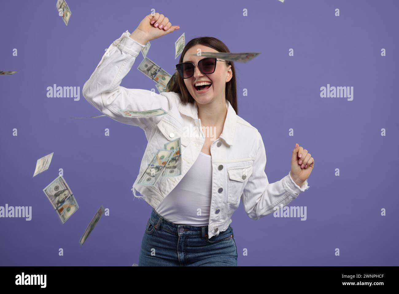 Happy woman under money shower on purple background Stock Photo