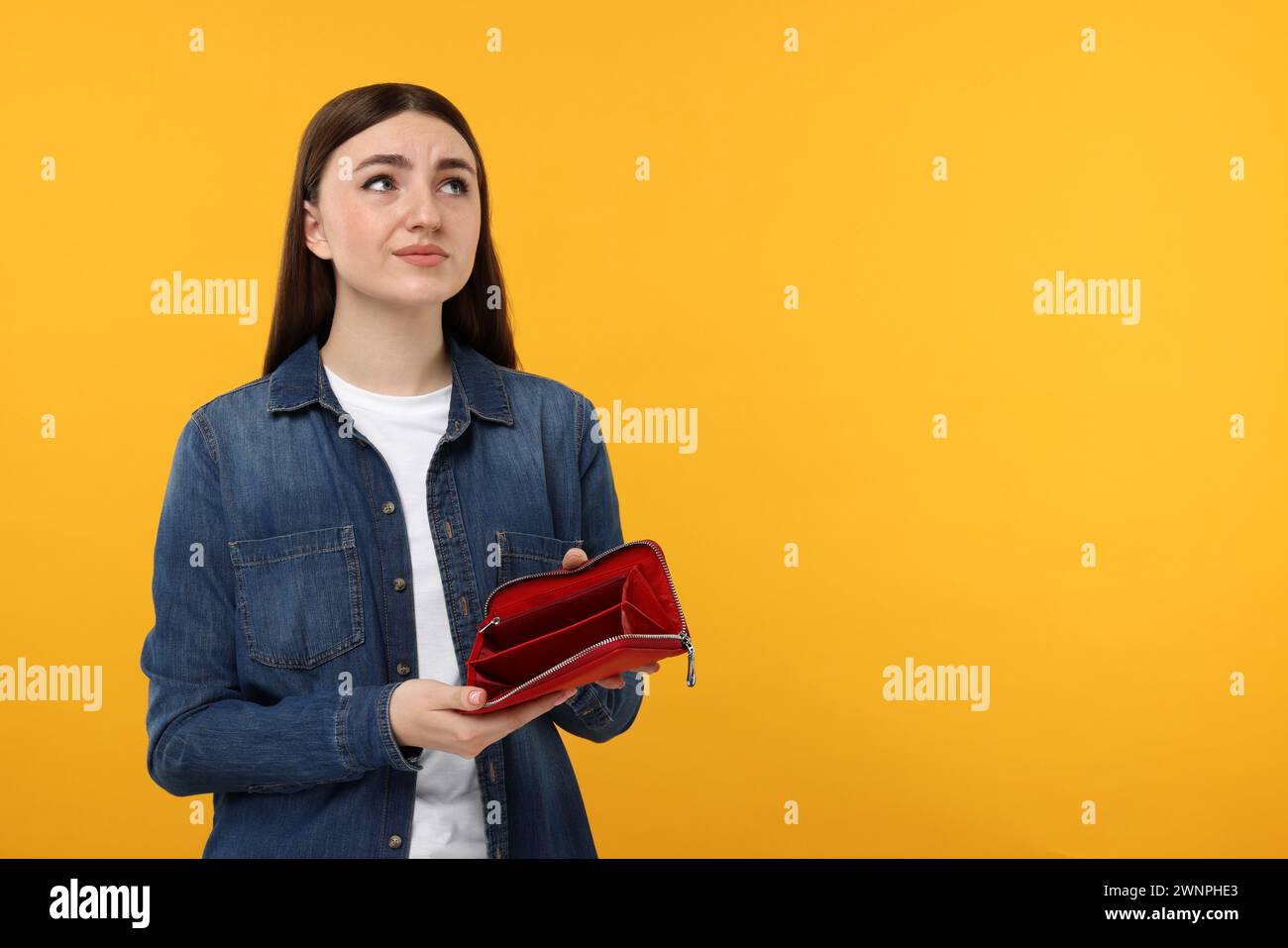 Sad woman showing empty wallet on orange background, space for text ...