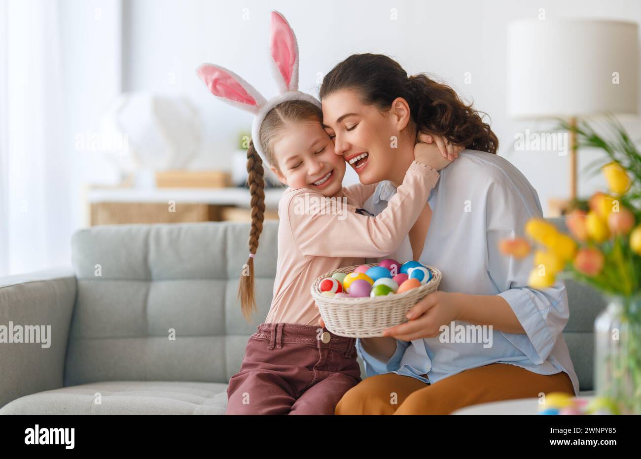 Happy holiday! Mother and her daughter with painting eggs. Family celebrating Easter. Cute little child girl is wearing bunny ears. Stock Photo