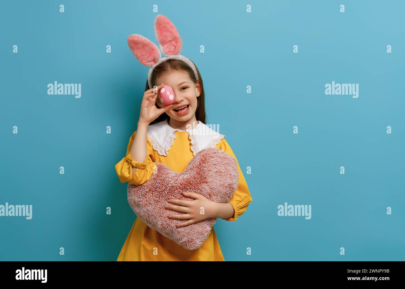 Cute little child wearing bunny ears on Easter day. Girl with painted egg. Stock Photo