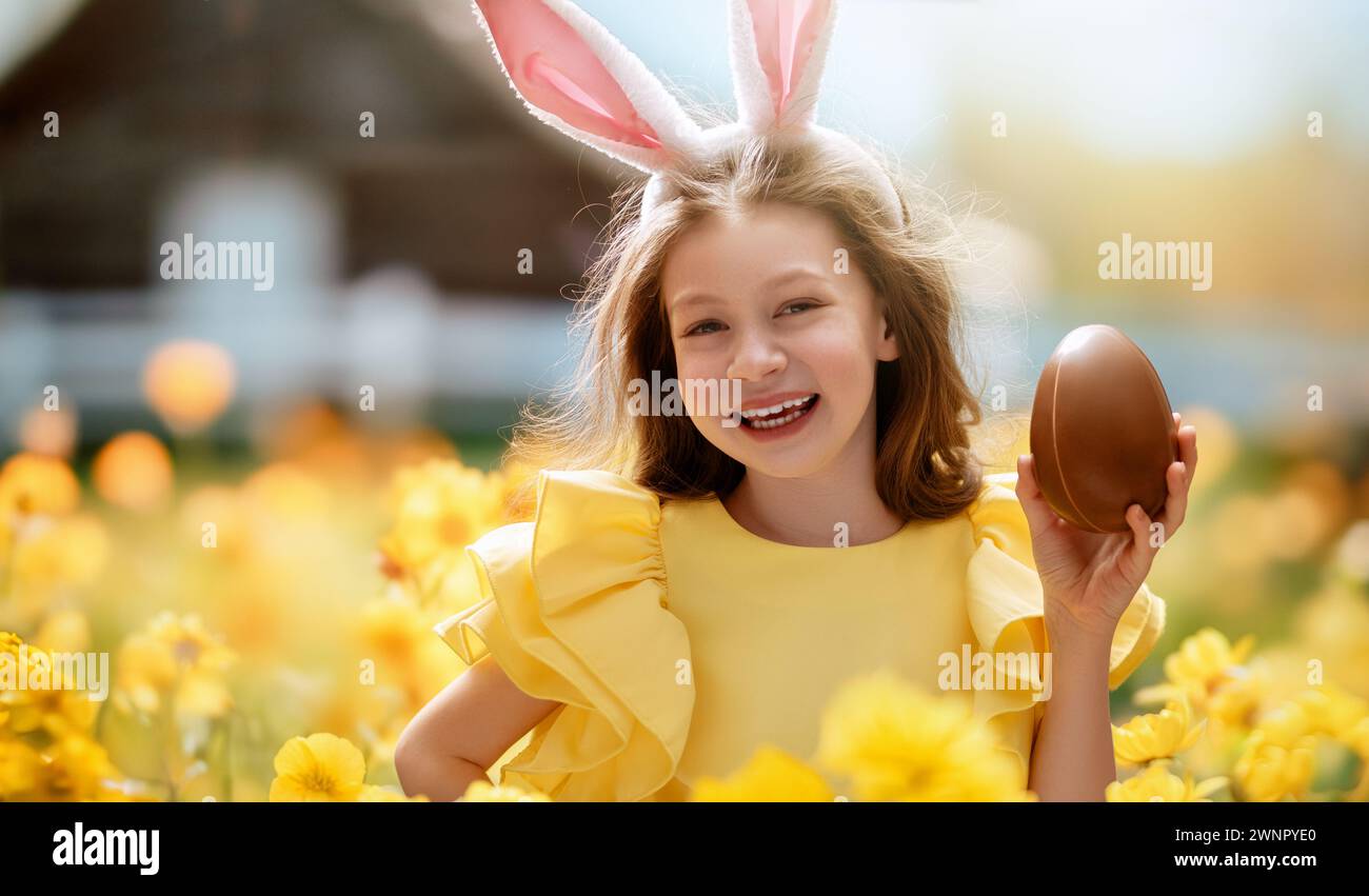 Beautiful child with chocolate egg outdoors. Happy family celebrating Easter in nature. Cute little girl is wearing bunny ears. Stock Photo