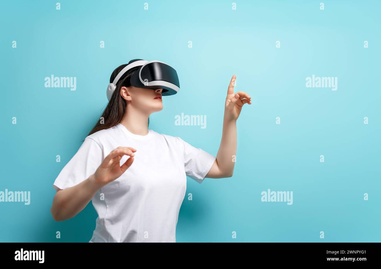 Metaverse technology concept. Woman with VR virtual reality goggles on light blue wall background. Futuristic lifestyle. Stock Photo