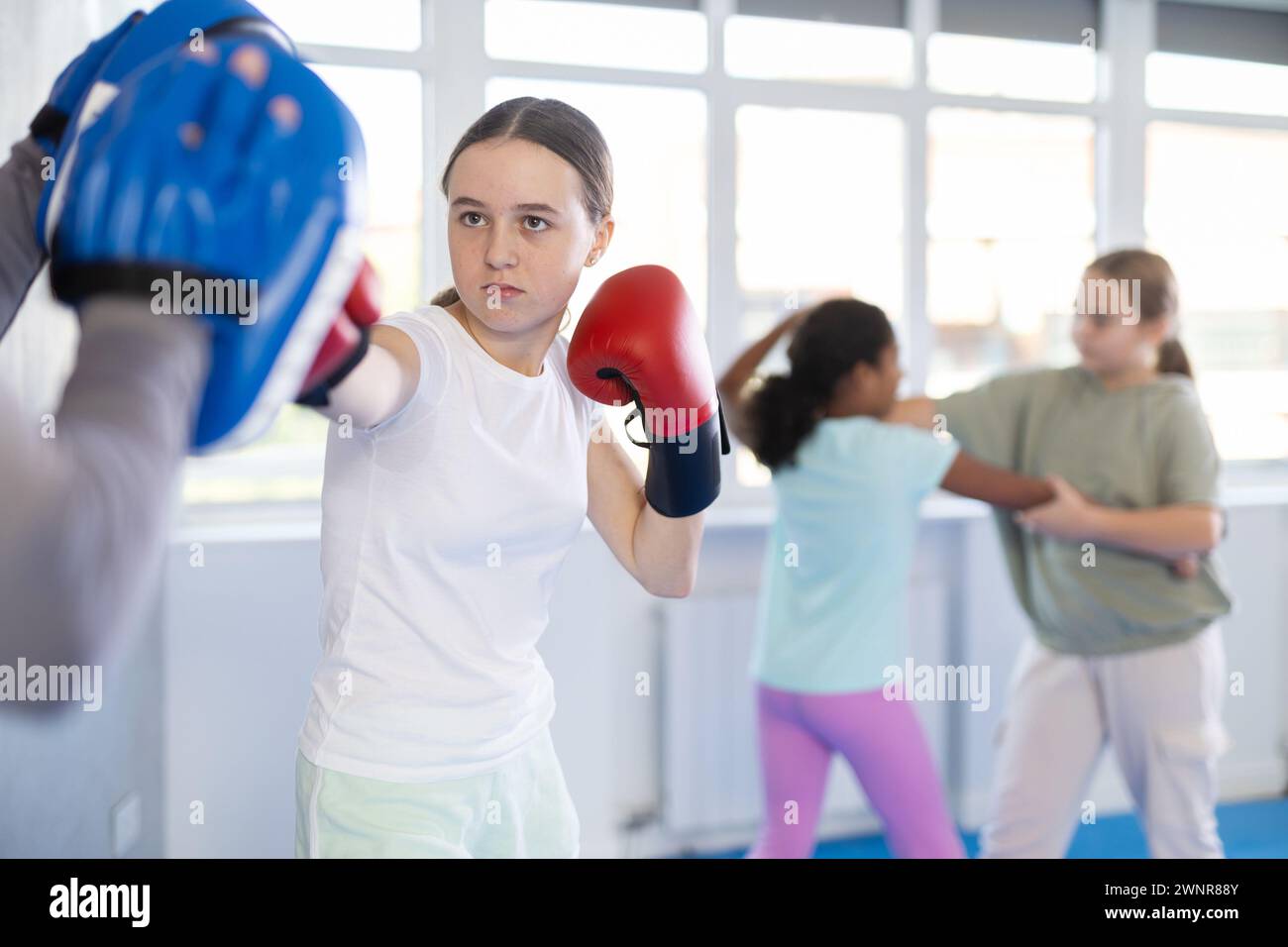 Focused girl hitting the focus mitts held by his boxing trainer in gym