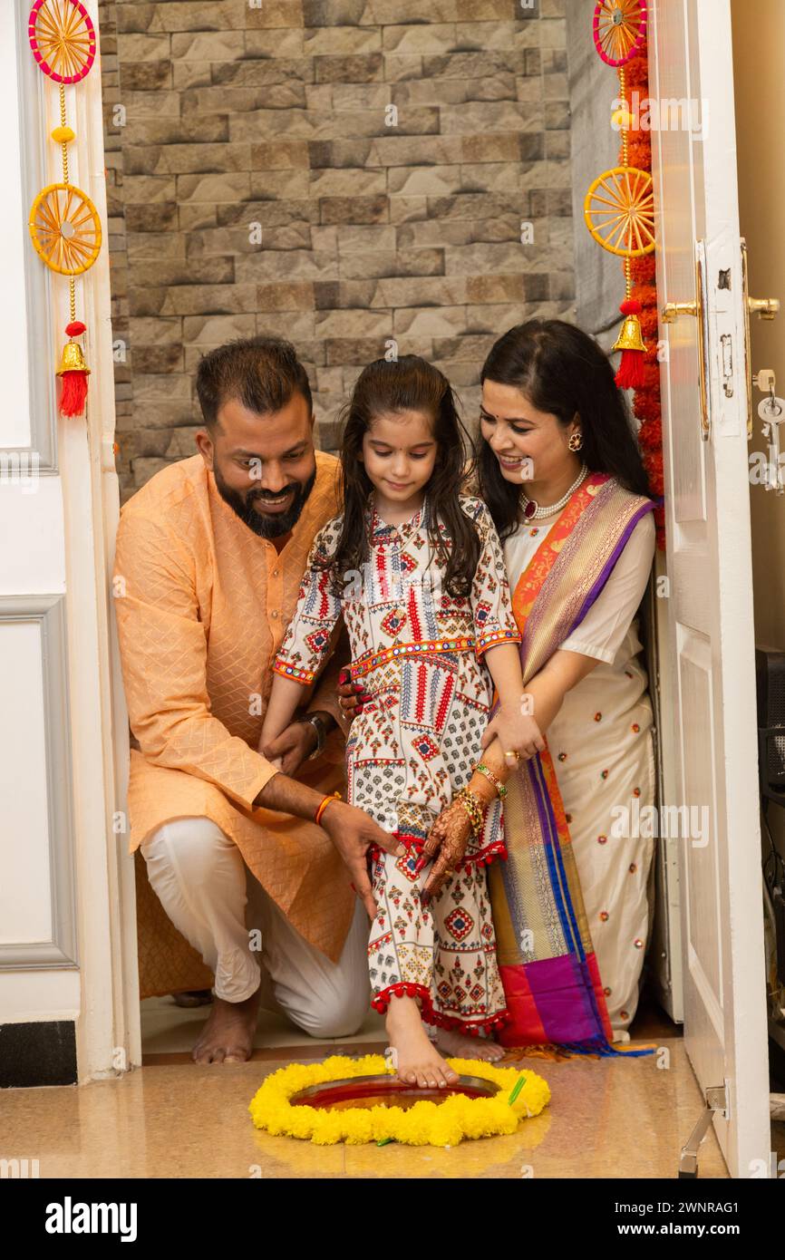 Happy indian family of three doing grah pravesh ritual or entering new house for the first time. daughter entering house with right feet stepping in a Stock Photo