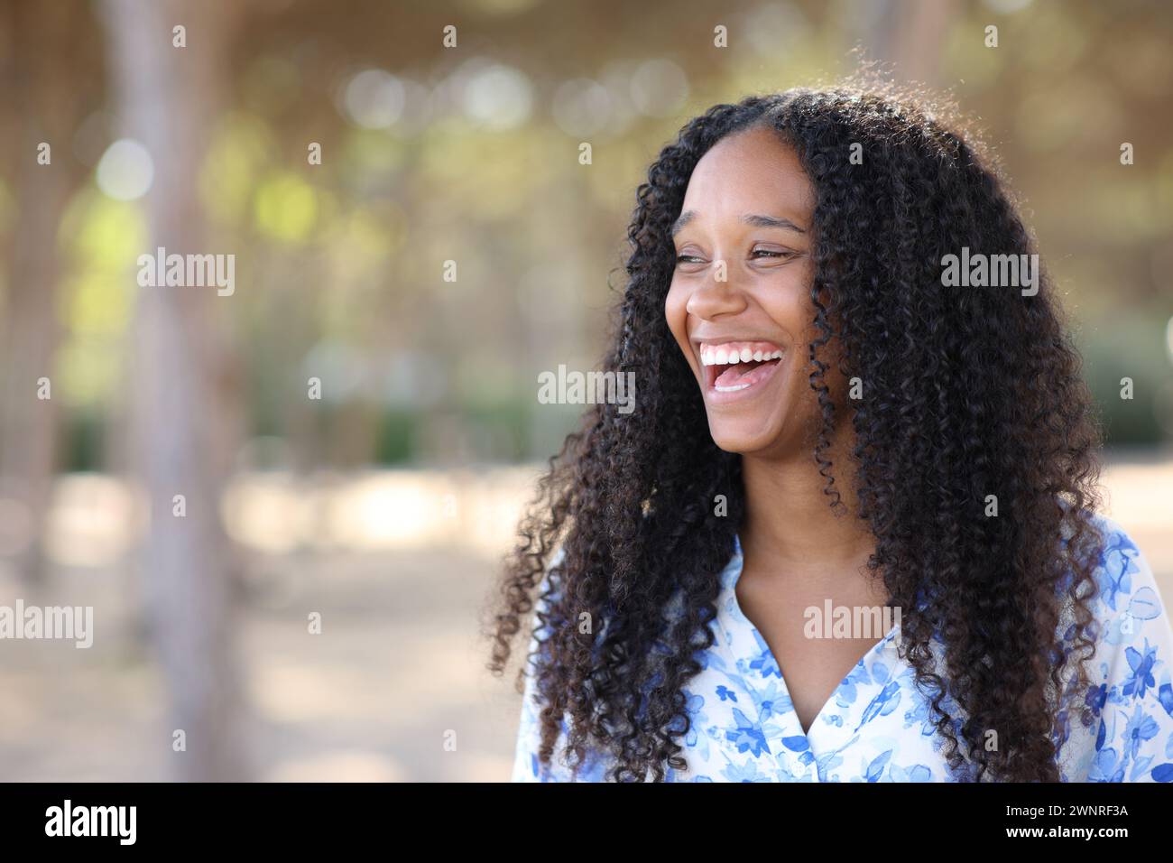 Joyful black woman laughing loud standing in a park looking at side Stock Photo