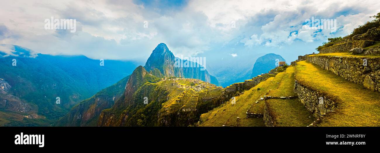 A wide 3:1 panorama photo with view over Machu Picchu, a 15th century Inca site located 2,430 meters above sea level on a mountain ridge above the Uru Stock Photo