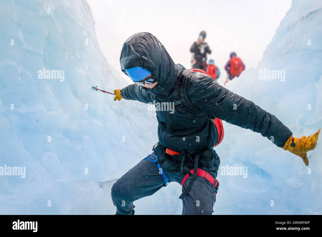 Man climbing down the glacier crevasse using ropes. Unrecognizable person taking photos using a smartphone. Exit Glacier ice hiking. Alaska. Stock Photo