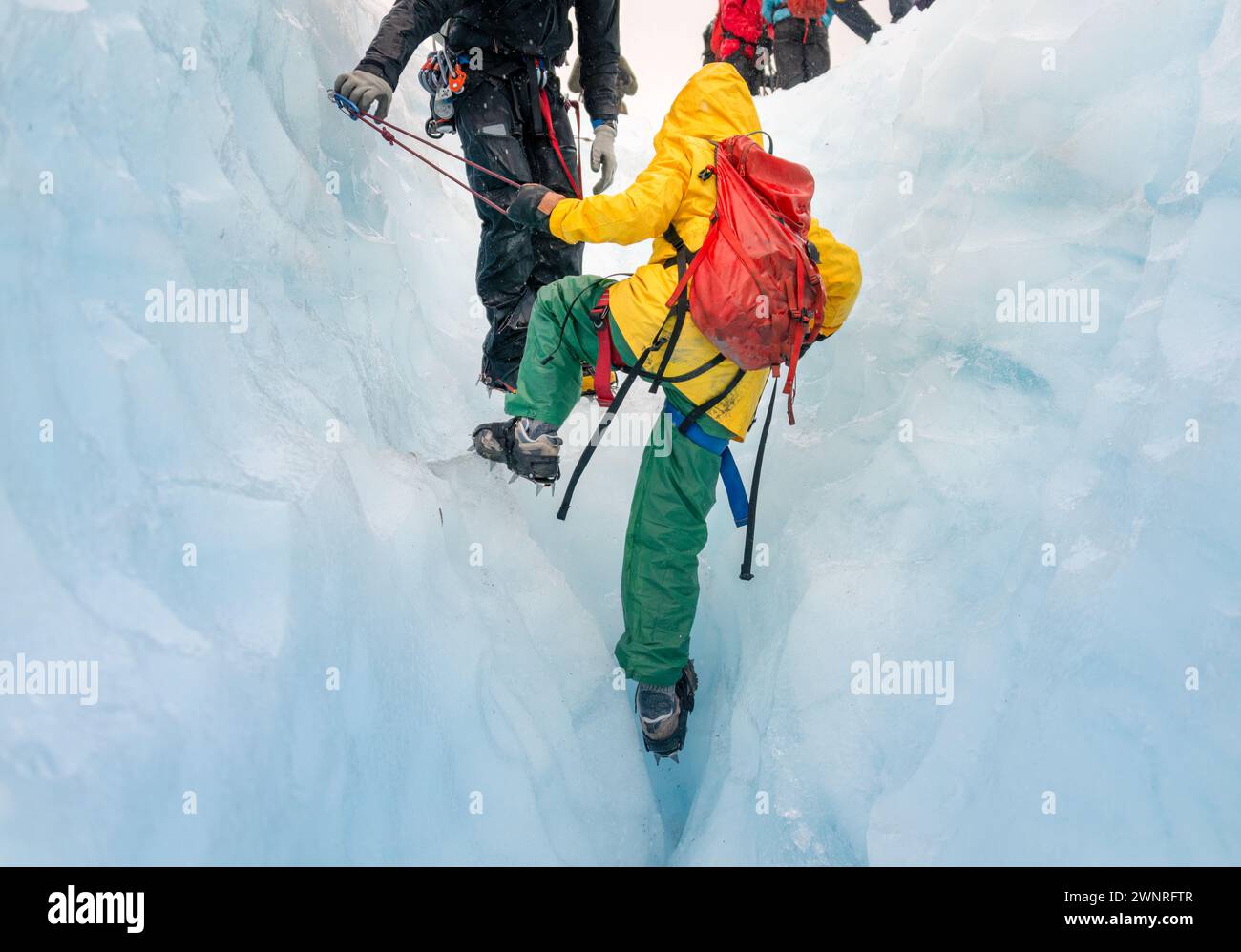 Unrecognizable tour guide helping woman climbing up glacier crevasse using ropes. Exit Glacier ice hiking. Alaska. Stock Photo