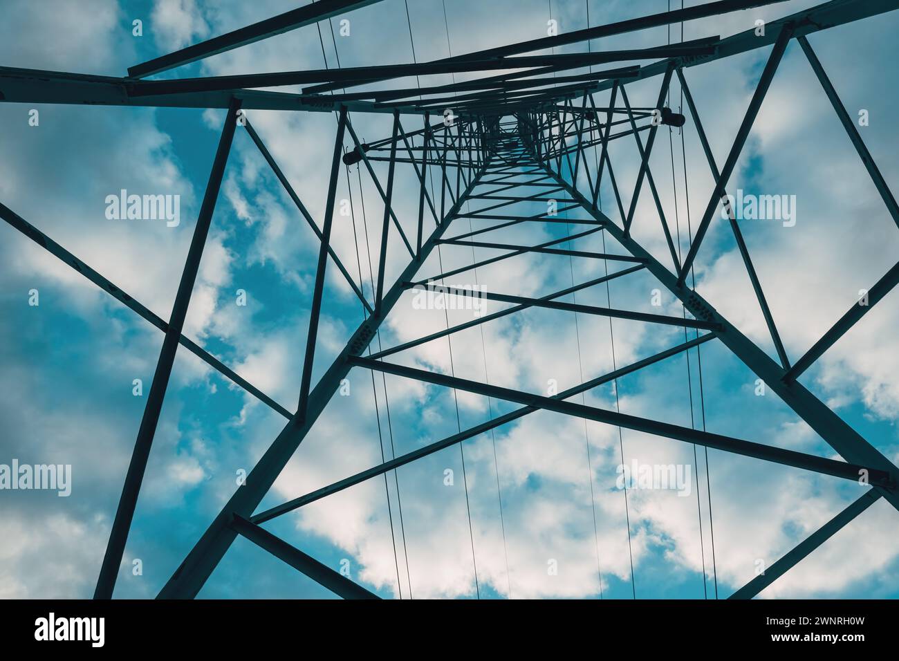 Electricity distribution tower from below, high voltage power lines under cloudy sky. Low angle view. Stock Photo