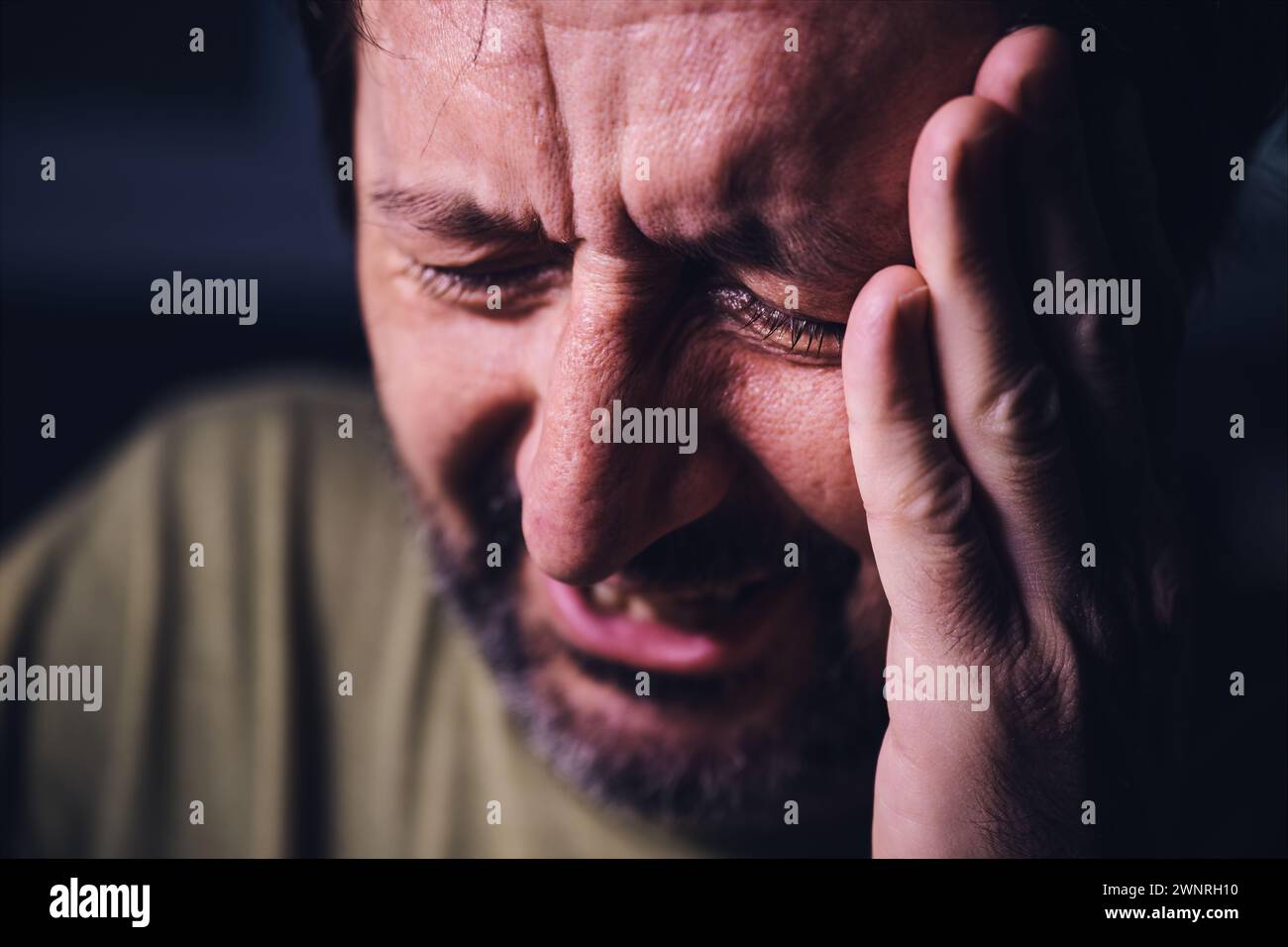 Grief and sadness, adult male crying in dark room, low key portrait with selective focus Stock Photo