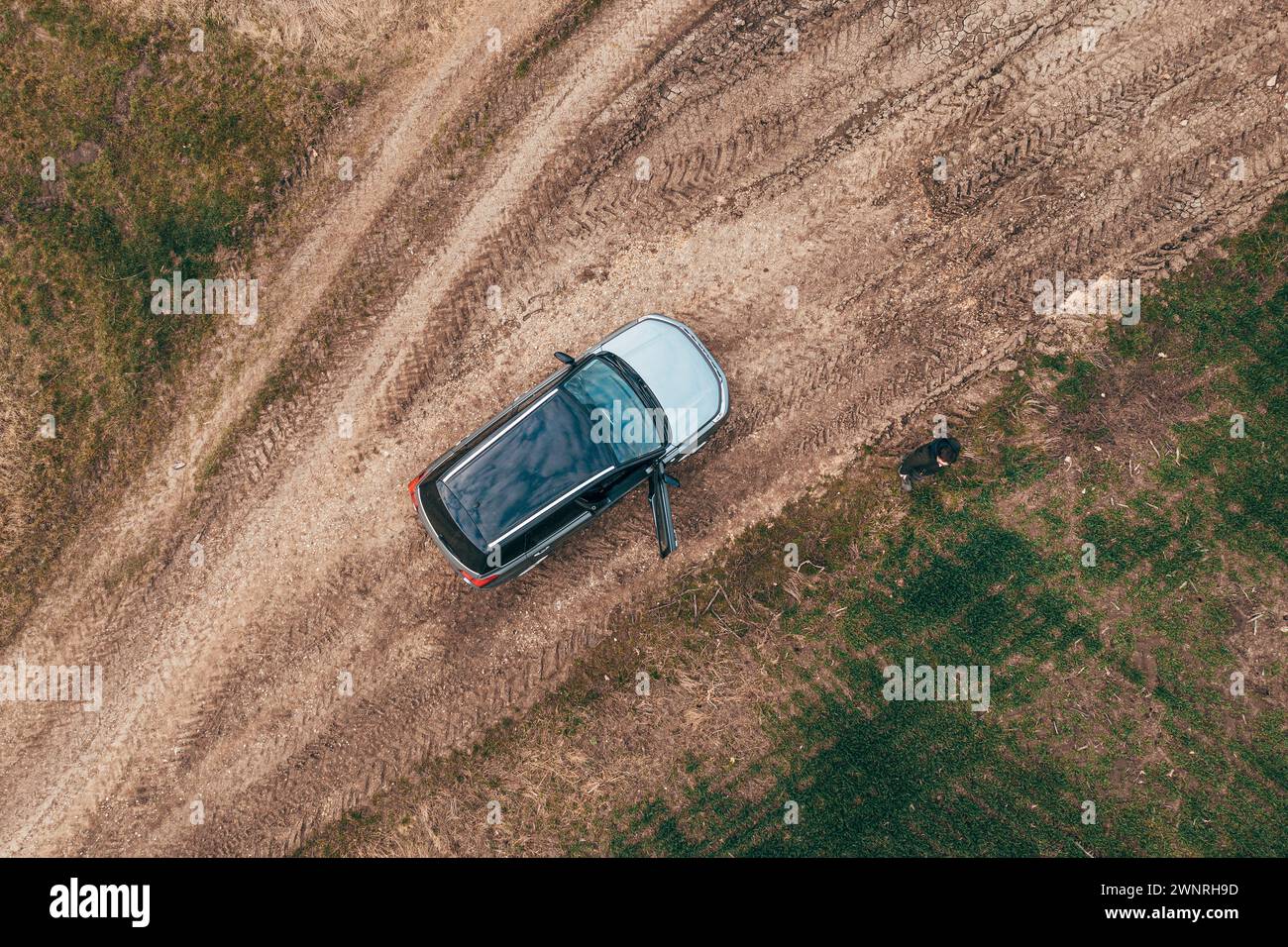 Man lost off-track on countryside road exiting out of the car and looking around, aerial shot from drone pov, top down Stock Photo