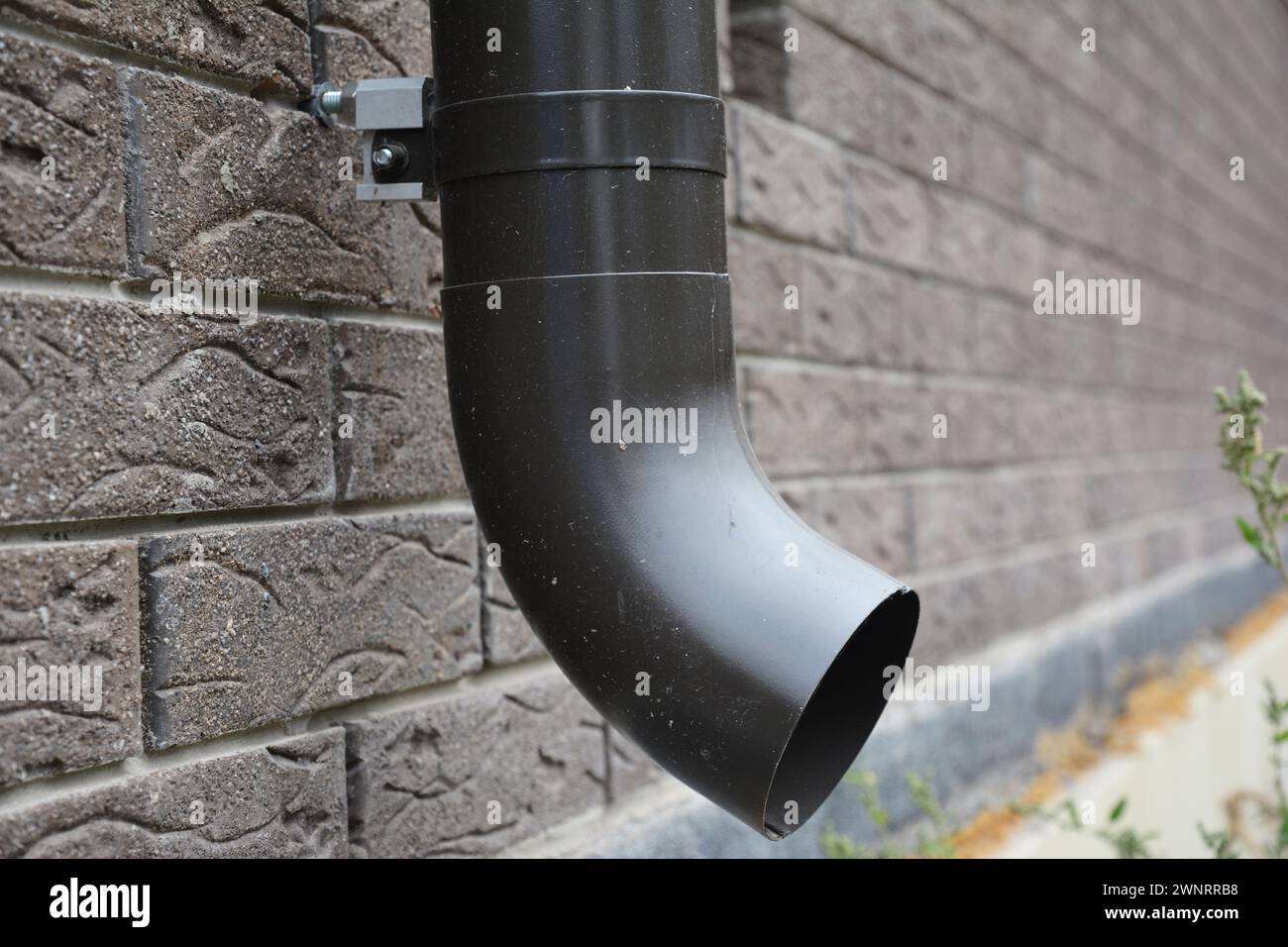 Metal rain gutter downspout pipe with anchor bolt holder on the house brick wall. Stock Photo