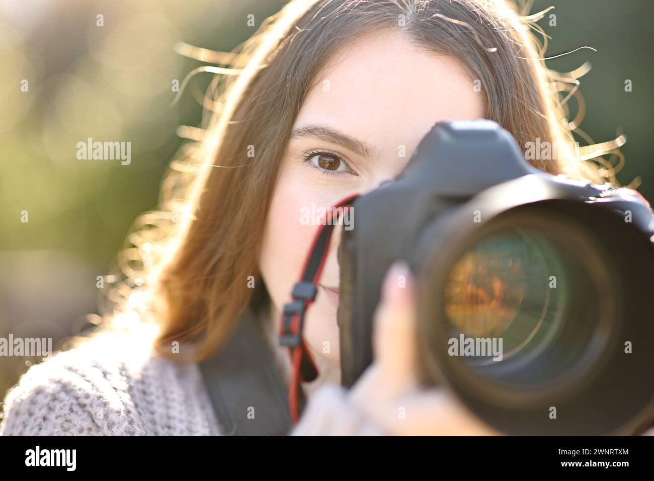 Front view of a photographer taking photo with dslr camera looking at you Stock Photo