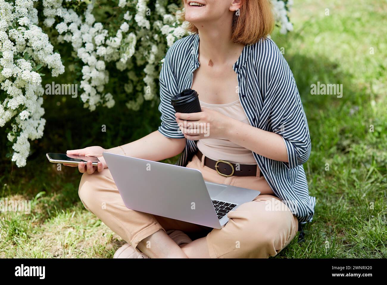 Freelance lifestyle with laptop, coffee and smartphone, woman surrounded by nature while working on her laptop. Stock Photo