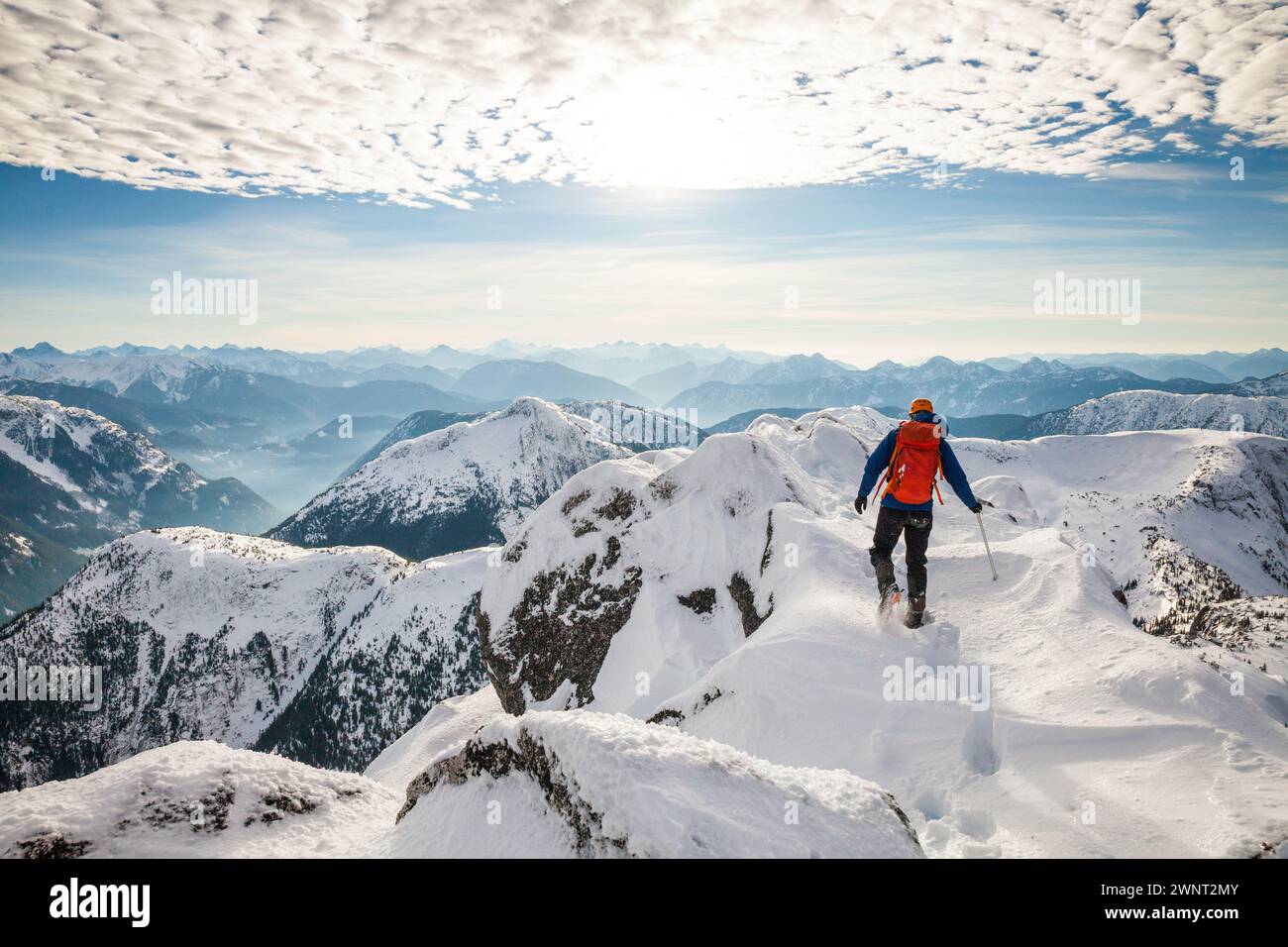 Mountaineer with backpack walks across mountain summit Stock Photo