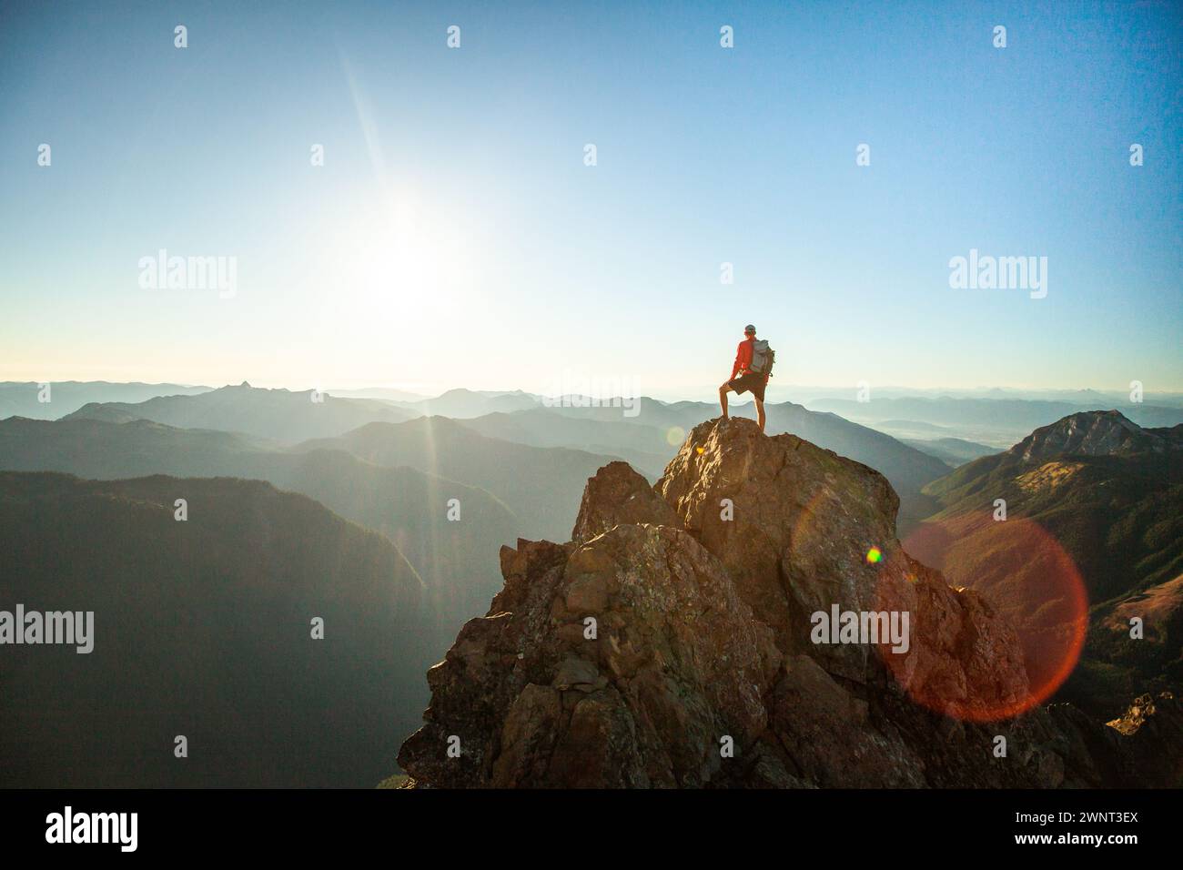 successful hiker wearing backpack stands on mountain summit, sunset Stock Photo