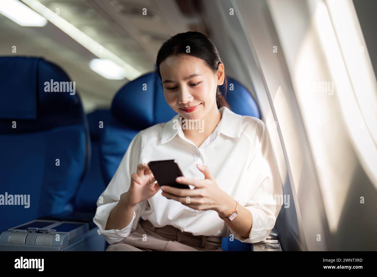 Traveling and technology. Flying at first class. Young business woman passenger using smartphone while sitting in airplane flight Stock Photo
