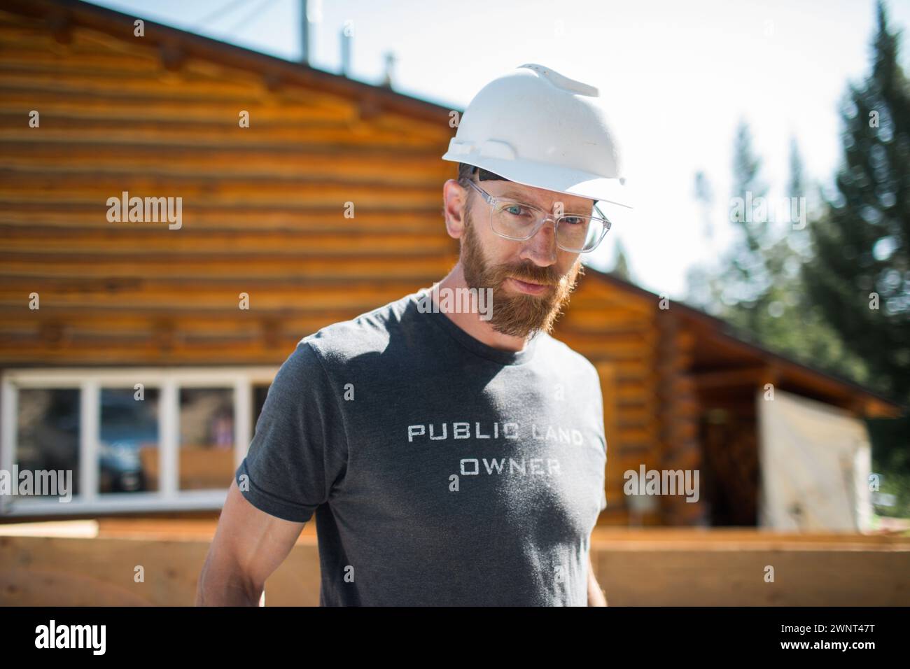 Bearded builder in safety gear by cabin. Stock Photo