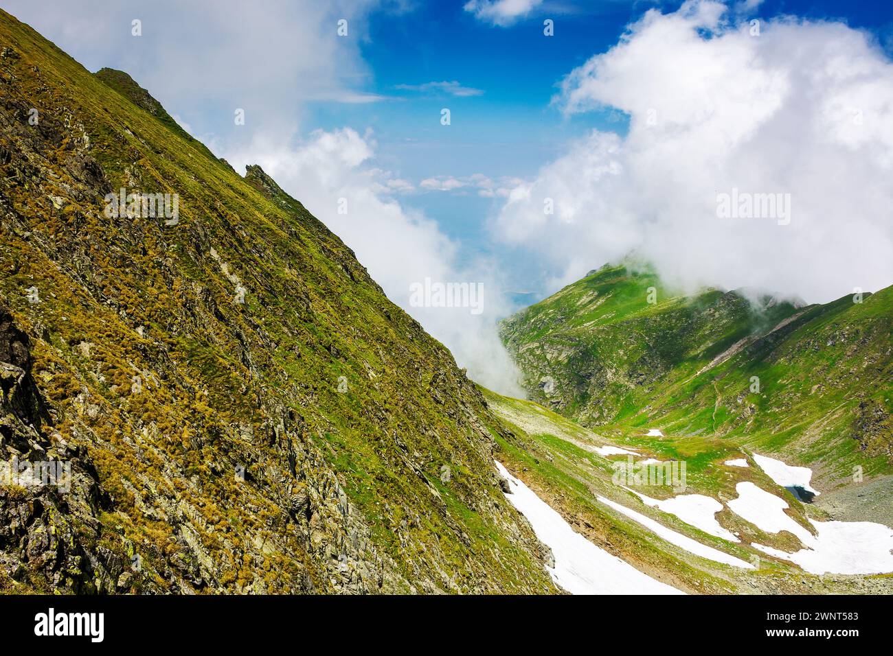 landscape of transylvania alps in summer. spots of snow among grass on the rocky hills of fagaras range beneath a sky with clouds. popular travel dest Stock Photo