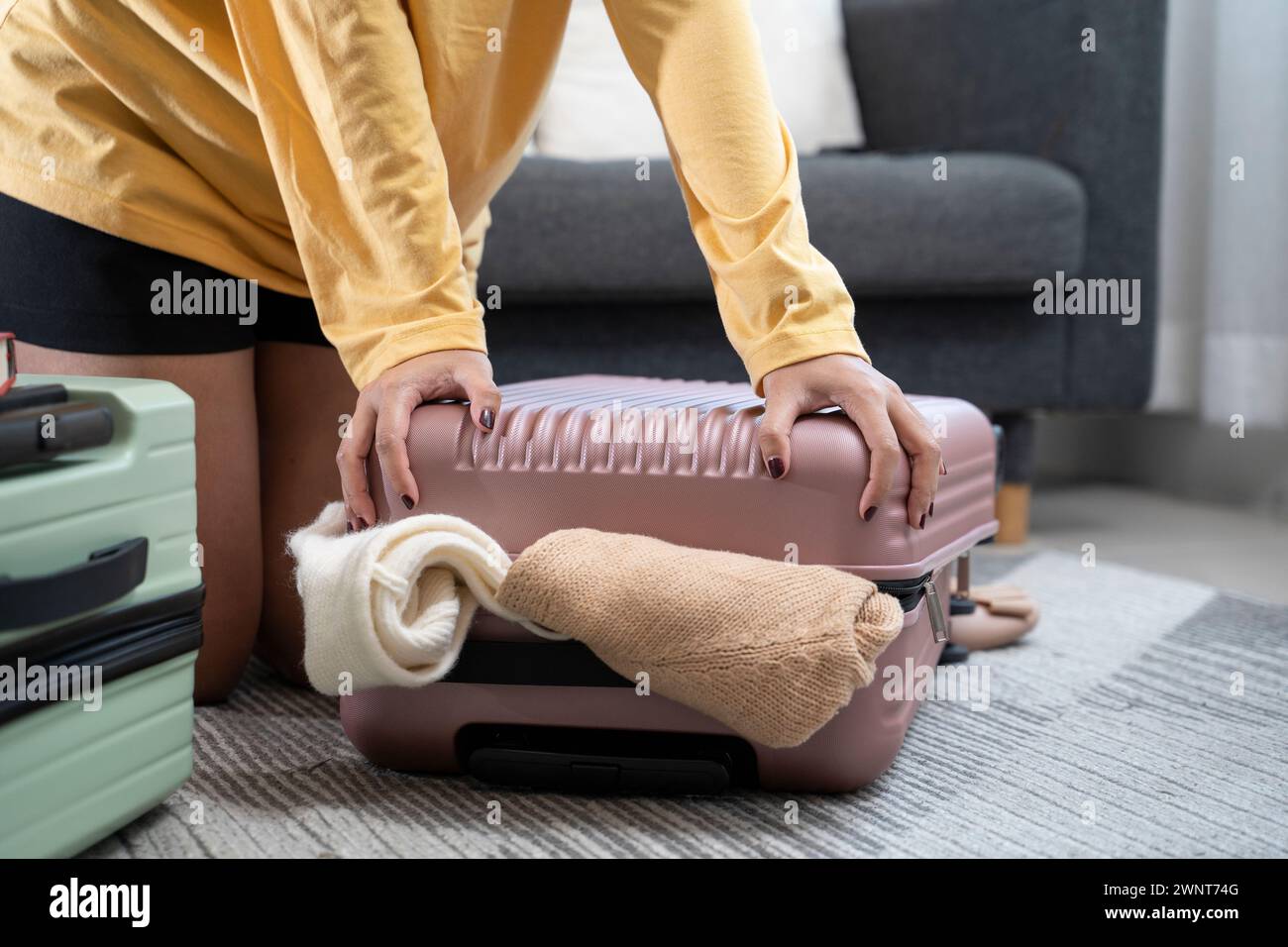 Asian young woman stacking clothes and into bag case, trying to pack hand luggage. Stock Photo