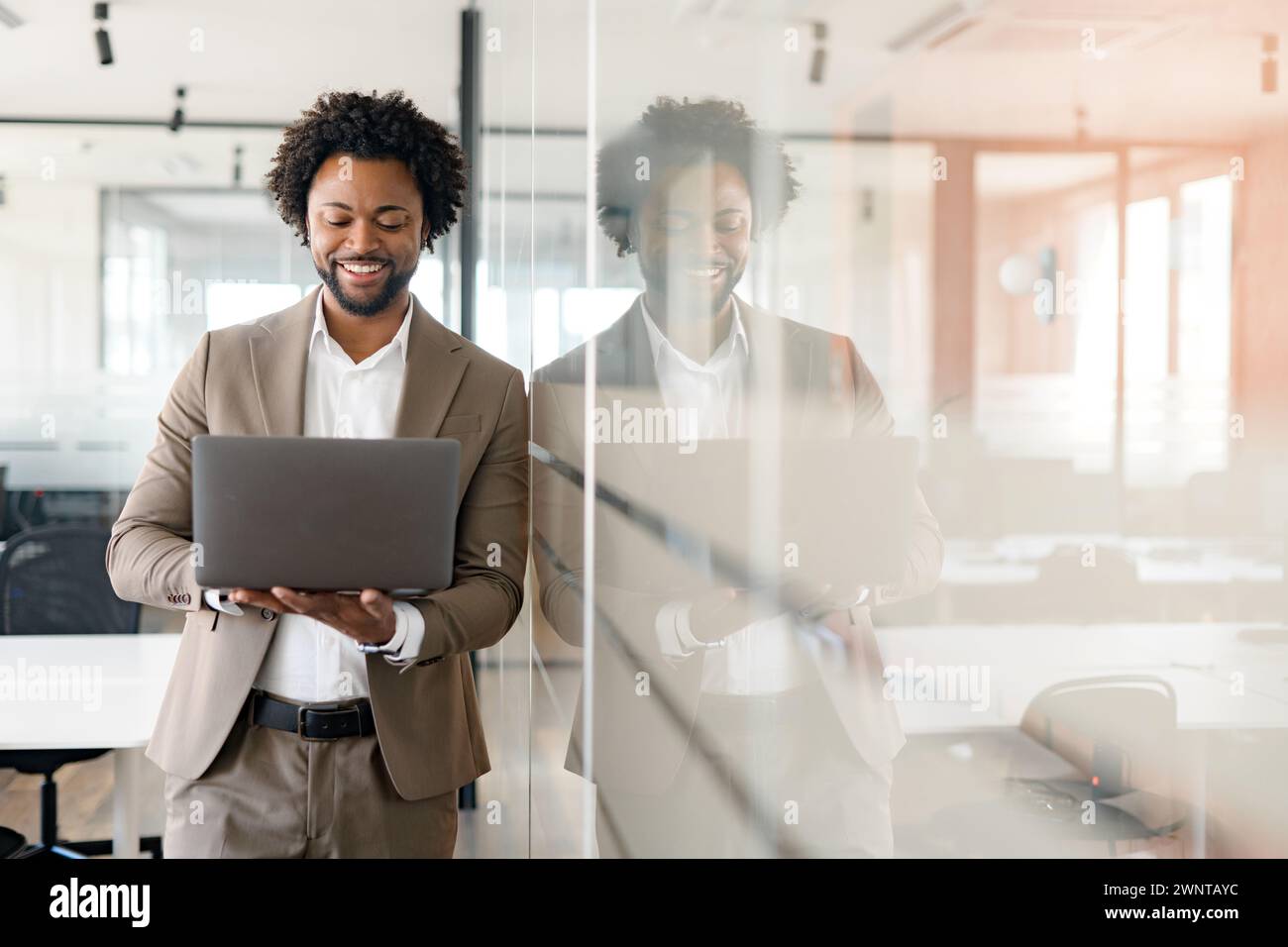 Professional businessman is immersed in laptop, smiling as he interacts with the content, encapsulating the joy of successful business endeavors and satisfaction of achieving goals in modern office Stock Photo