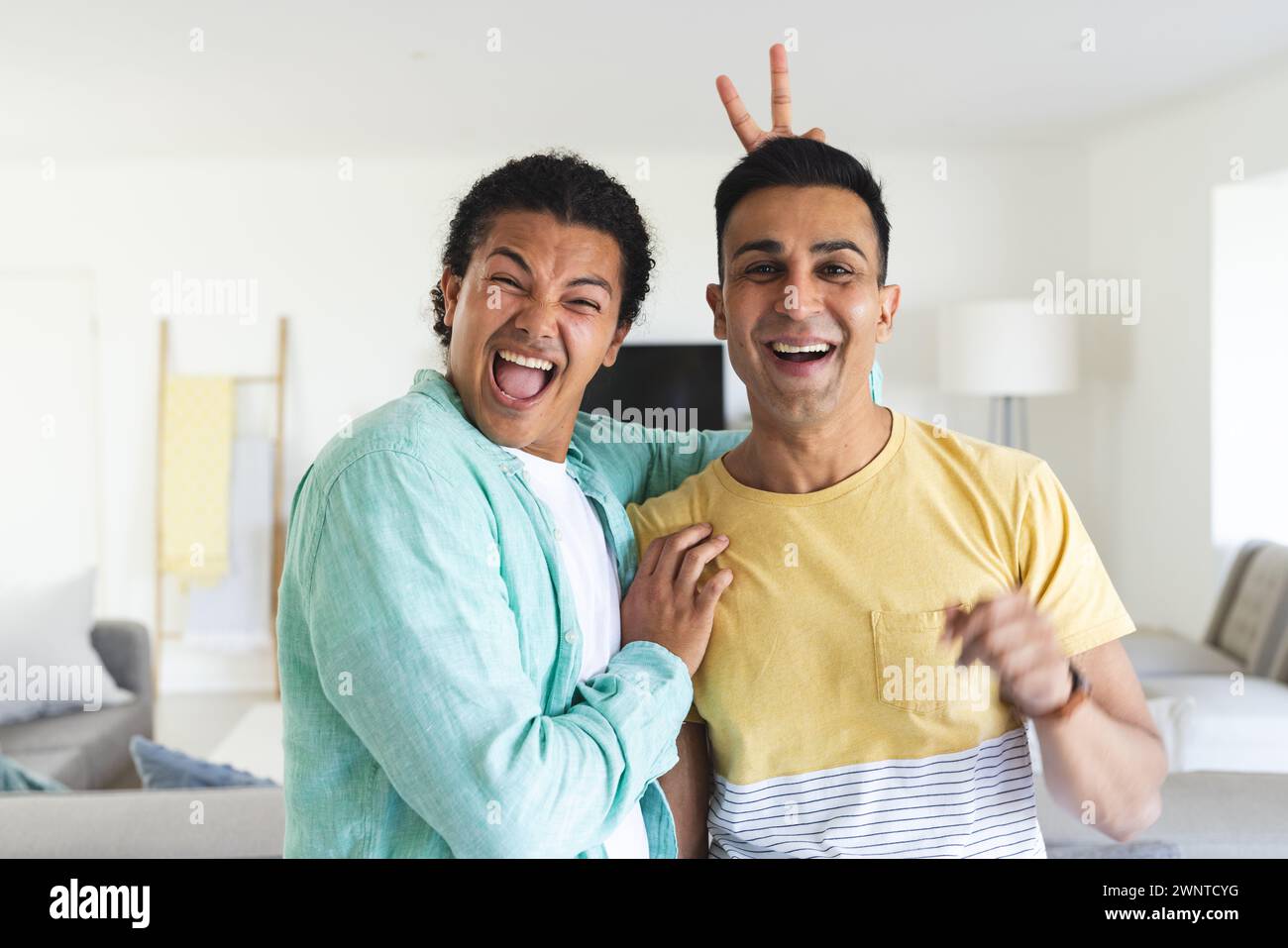 Young biracial man playfully gives a peace sign behind the head of a smiling Middle Eastern man Stock Photo