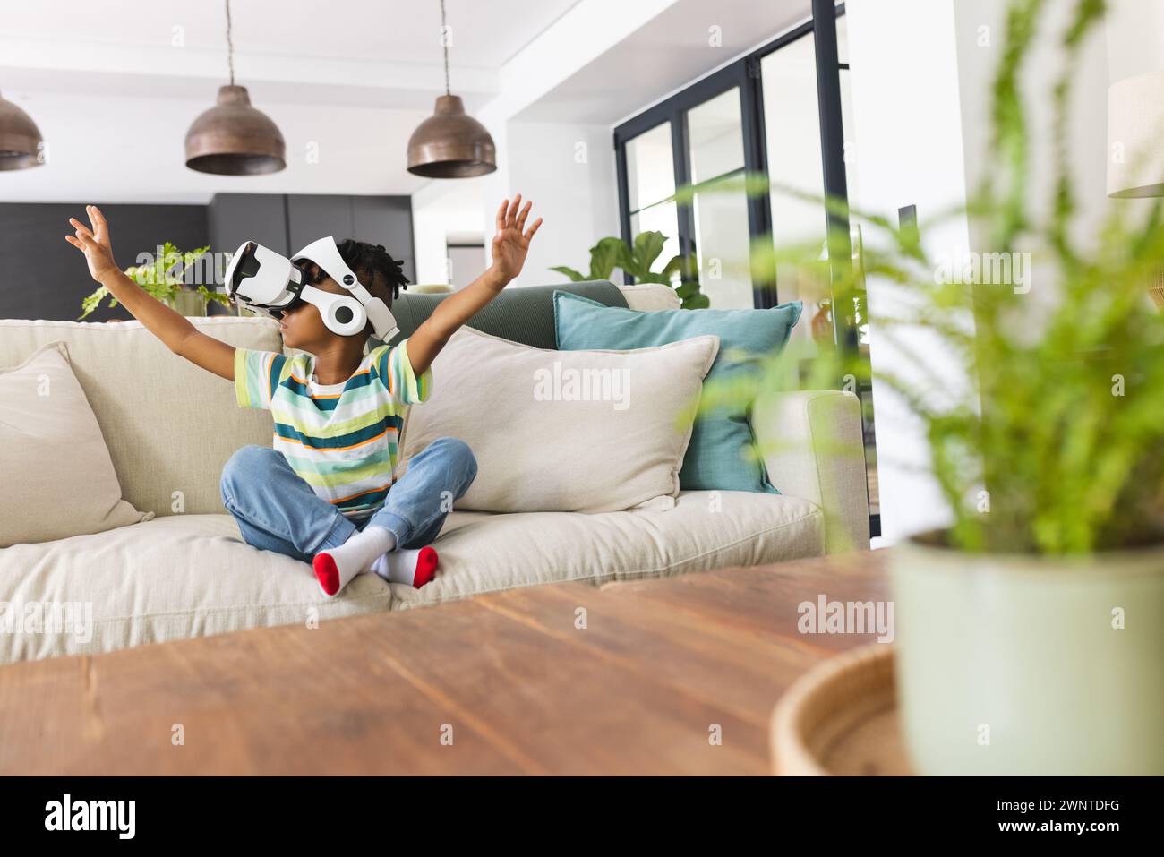 African American boy enjoys a virtual reality headset, arms raised in excitement Stock Photo