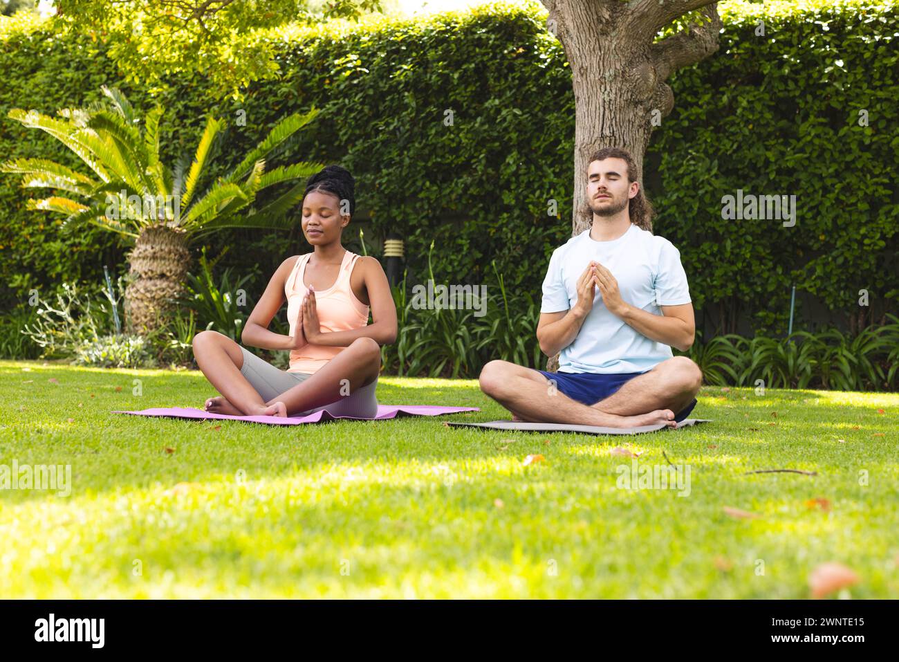 Diverse couple meditates in serene garden, embracing tranquility. Stock Photo