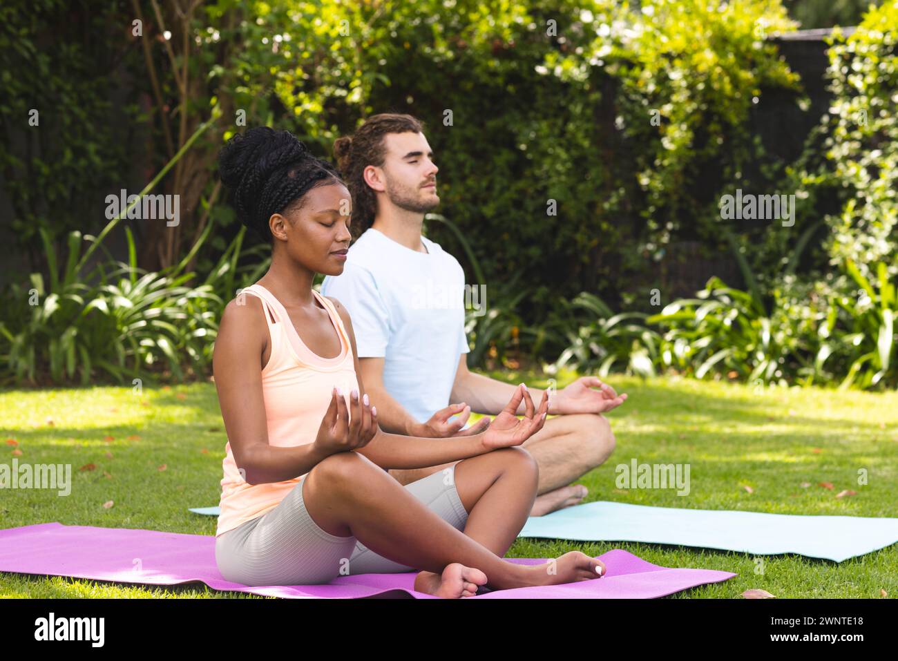 Diverse couple, a young African American woman and young Caucasian man, practice yoga outdoors Stock Photo