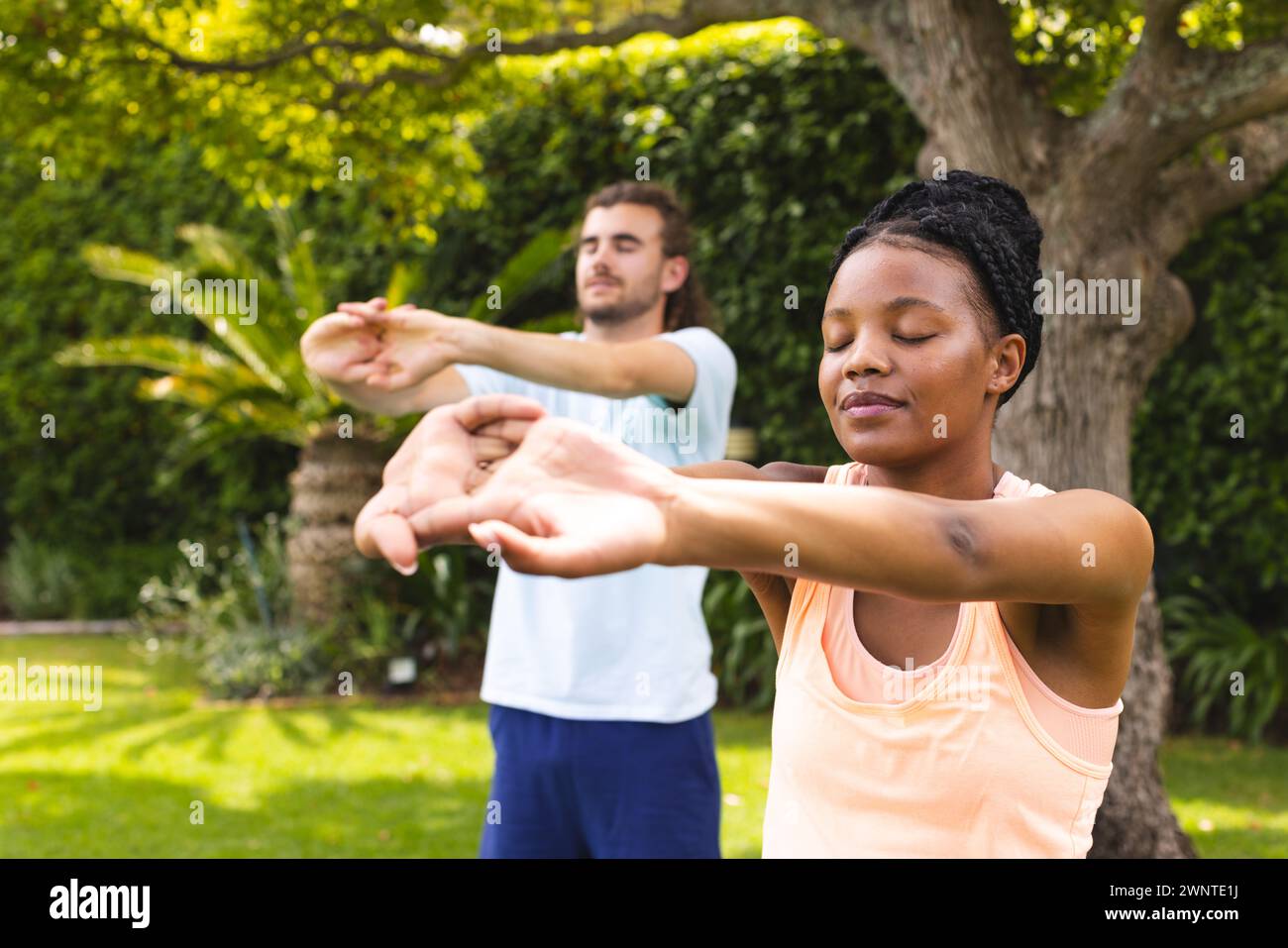 Diverse couple, a young African American woman and Caucasian man, practice yoga outdoors Stock Photo