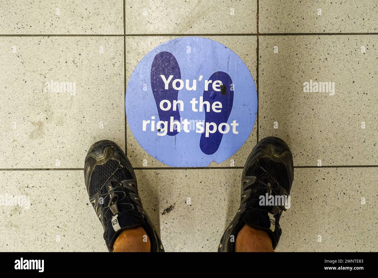 Feet above the Schiphol airport floor, with a 'You're on the right spot' sign, during covid lockdown restrictions for social distancing Stock Photo