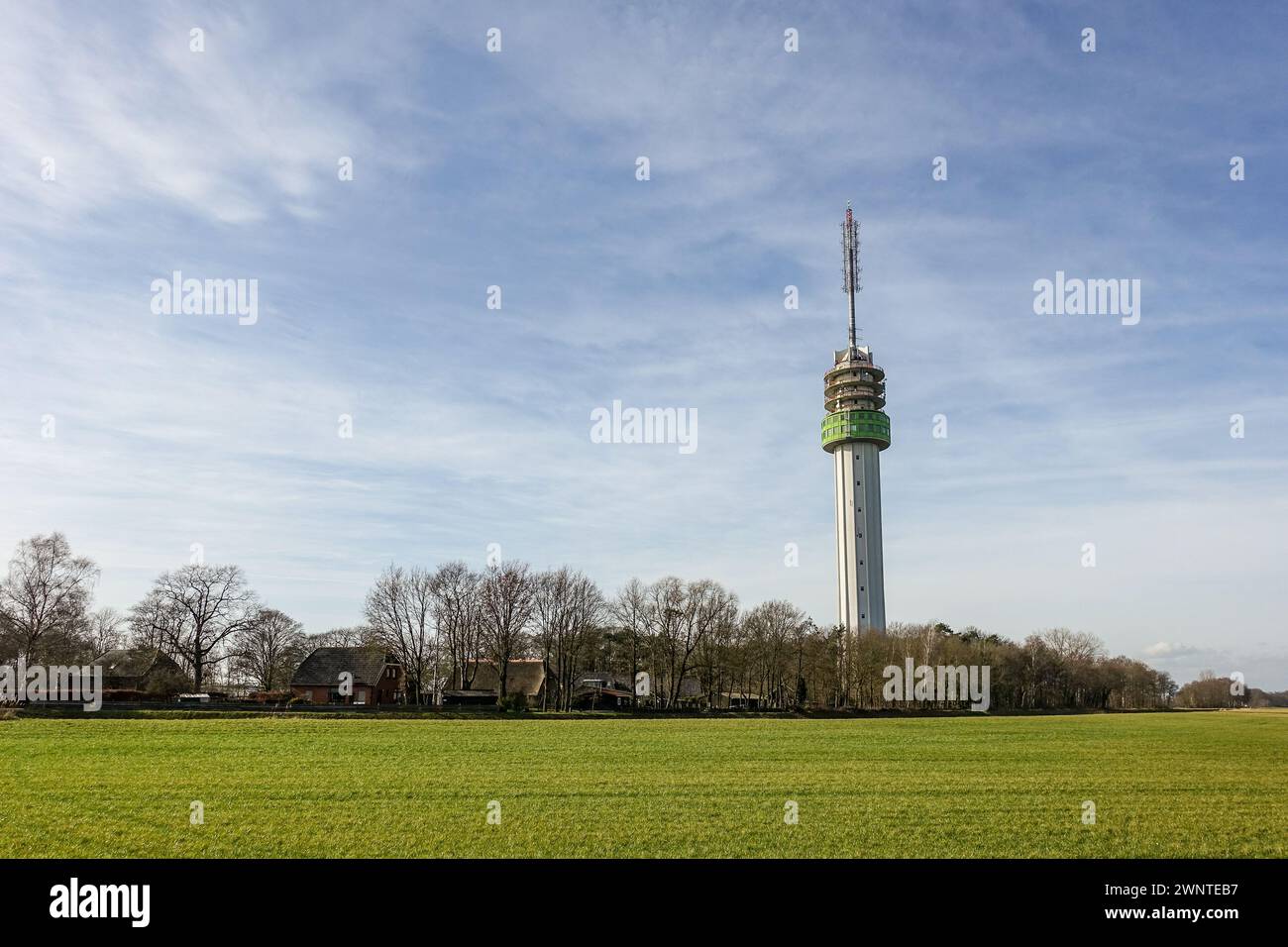 A telecommunications tower (Zendmast Markelo, tallest building in Overijssel) with antennas and dishes against a clear blue sky, surrounded by trees. Stock Photo