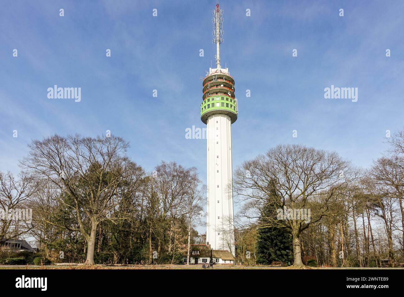 A telecommunications tower (Zendmast Markelo, tallest building in Overijssel) with antennas and dishes against a clear blue sky, surrounded by trees. Stock Photo