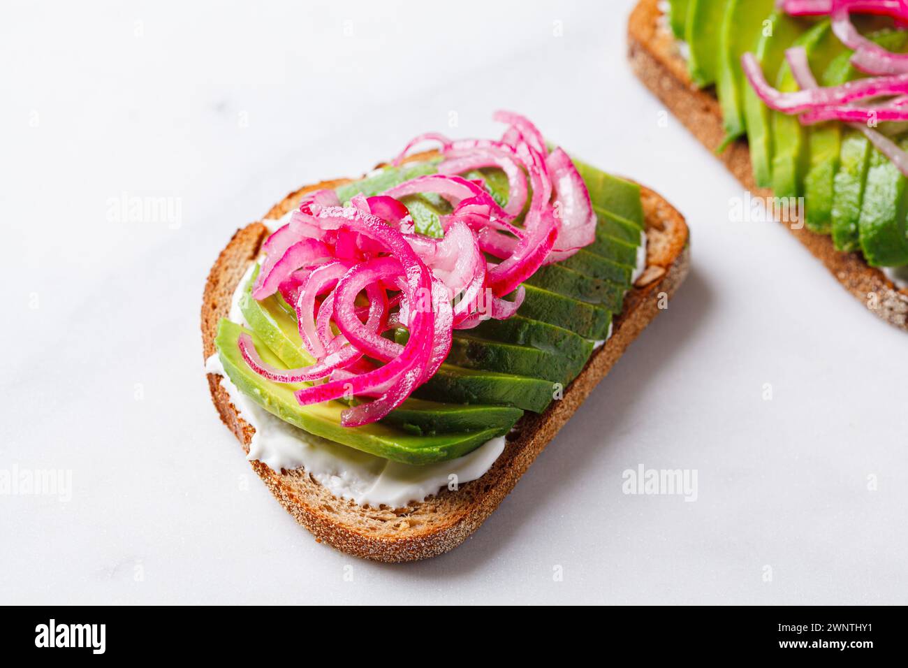 Avocado toast with cream cheese and pickled onions on a white plate. Stock Photo
