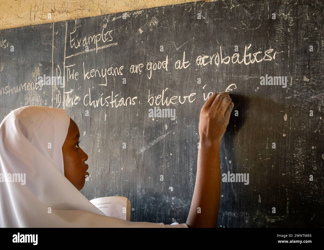 A muslim girl student writes 'Christians believe in God' on a blackboard, Jambiani Secondary School, Zanzibar, Tanzania Stock Photo