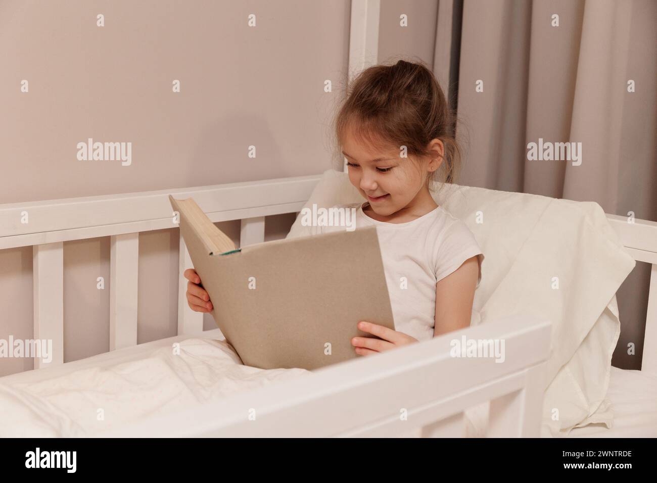 cute little girl sitting in bed and reading book Stock Photo - Alamy
