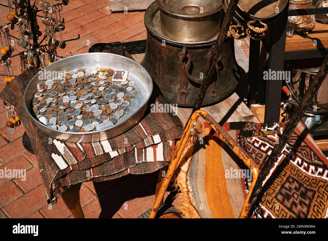 Vintage coins in a metal tray, rusty old cauldron and pots, key chains, rug and other goods in a shop at bazaar. Stock Photo