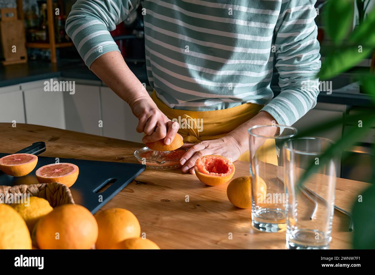 Female hands making homemade grapefruit juice with hand citrus juicer. Anonymous woman preparing fresh grapefruit juice in the kitchen. Stock Photo