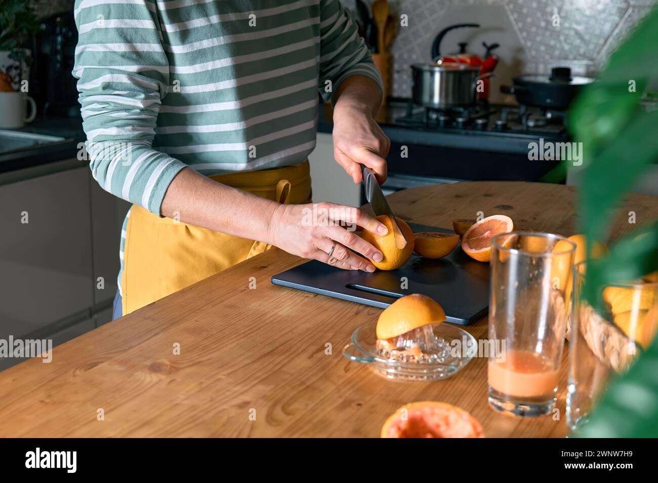 Female hands making homemade grapefruit juice with hand citrus juicer. Anonymous woman cutting ripe grapefruit in half for preparing fresh grapefruit Stock Photo