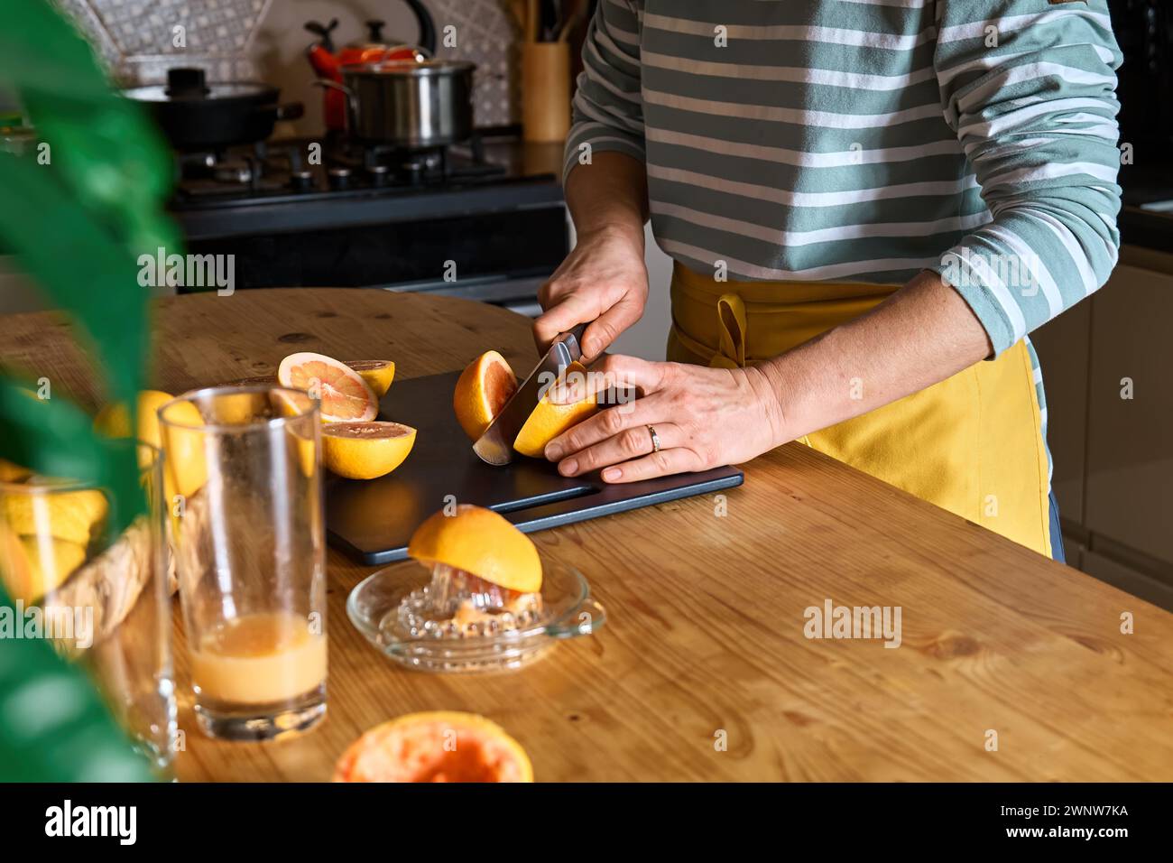 Female hands making homemade grapefruit juice with hand citrus juicer. Anonymous woman cutting ripe grapefruit in half for preparing fresh grapefruit Stock Photo