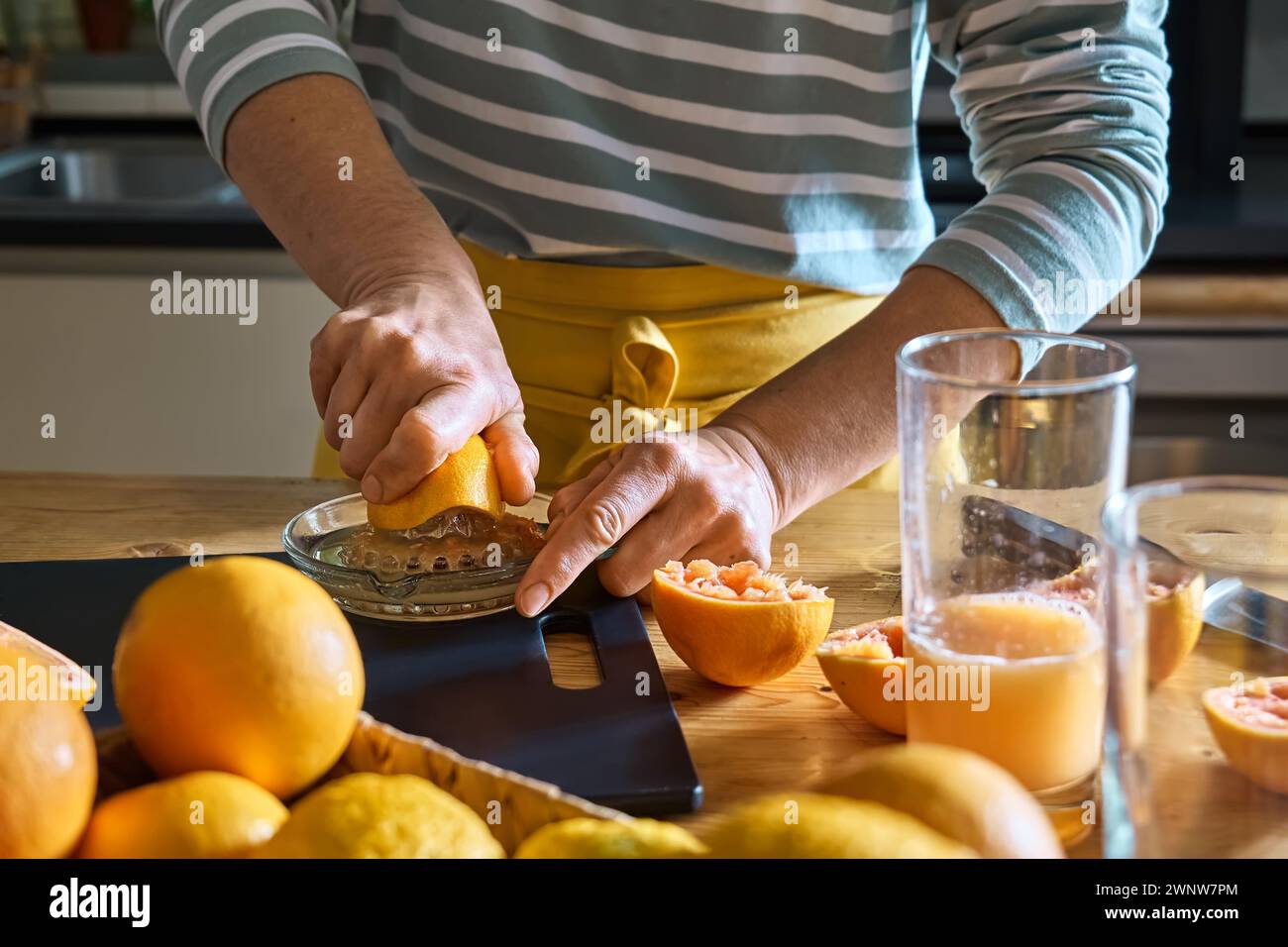 Female hands making homemade grapefruit juice with hand citrus juicer. Anonymous woman preparing fresh grapefruit juice in the kitchen. Stock Photo