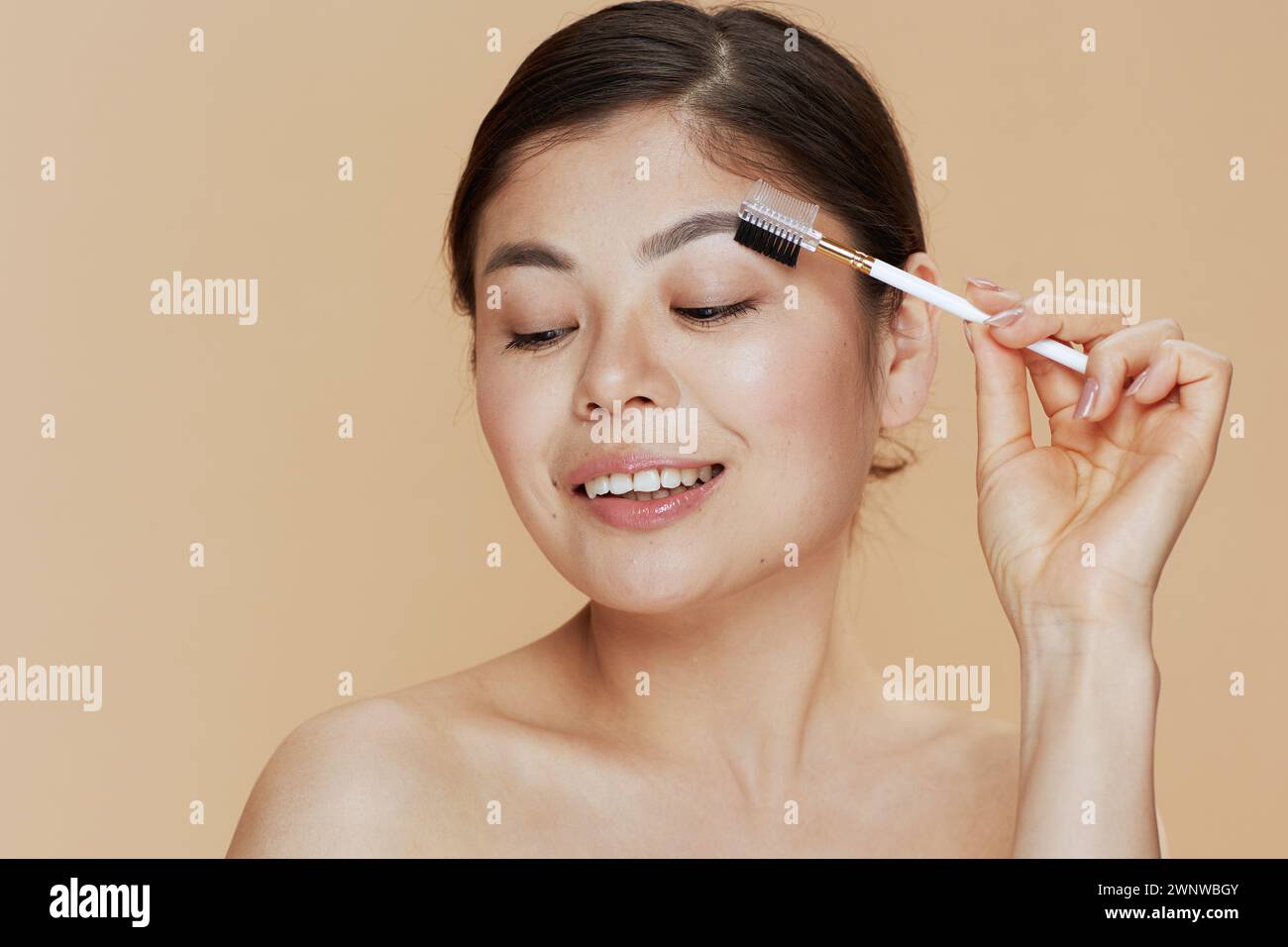 young asian woman with brow brush on beige background. Stock Photo