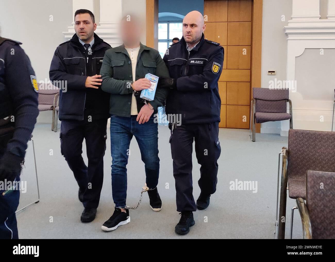 04 March 2024, Baden-Württemberg, Ellwangen: One of the defendants, who is wearing an ankle bracelet, is brought into the courtroom of the district court by judicial officers. The Federal Criminal Police Office and the Ellwangen public prosecutor's office had uncovered a large drug laboratory for Captagon in Regensburg in July. At the time, the Federal Criminal Police Office and the public prosecutor's office spoke of the largest known drug laboratory for Captagon in Germany. Now the trial of two defendants has begun. Photo: Katharina Schröder/dpa - ATTENTION: The defendant has been pixelated Stock Photo