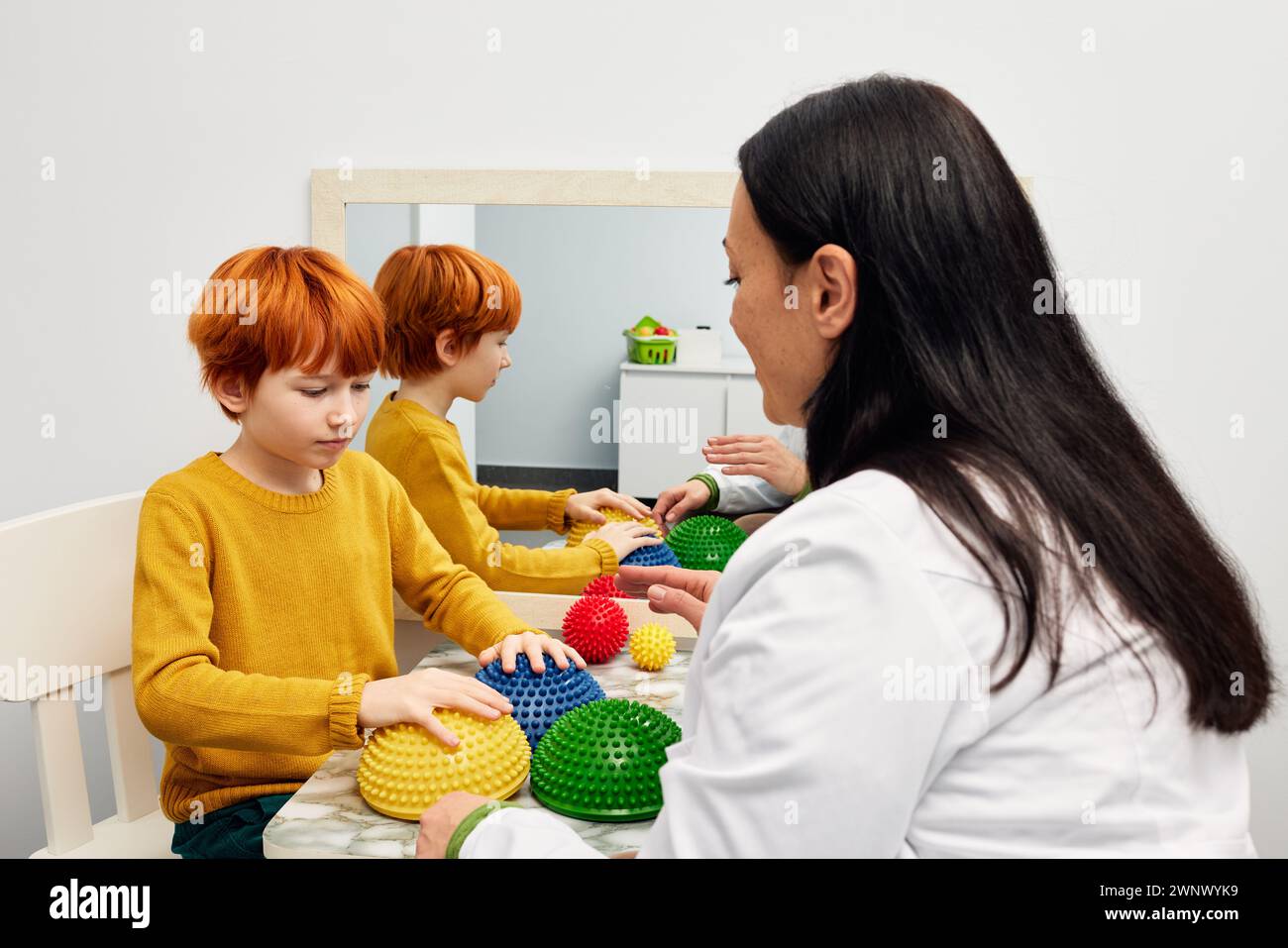 Occupational therapist using sensory integration therapy to improve sensory processing for male child patient. doctor using hedgehog half balls to dev Stock Photo