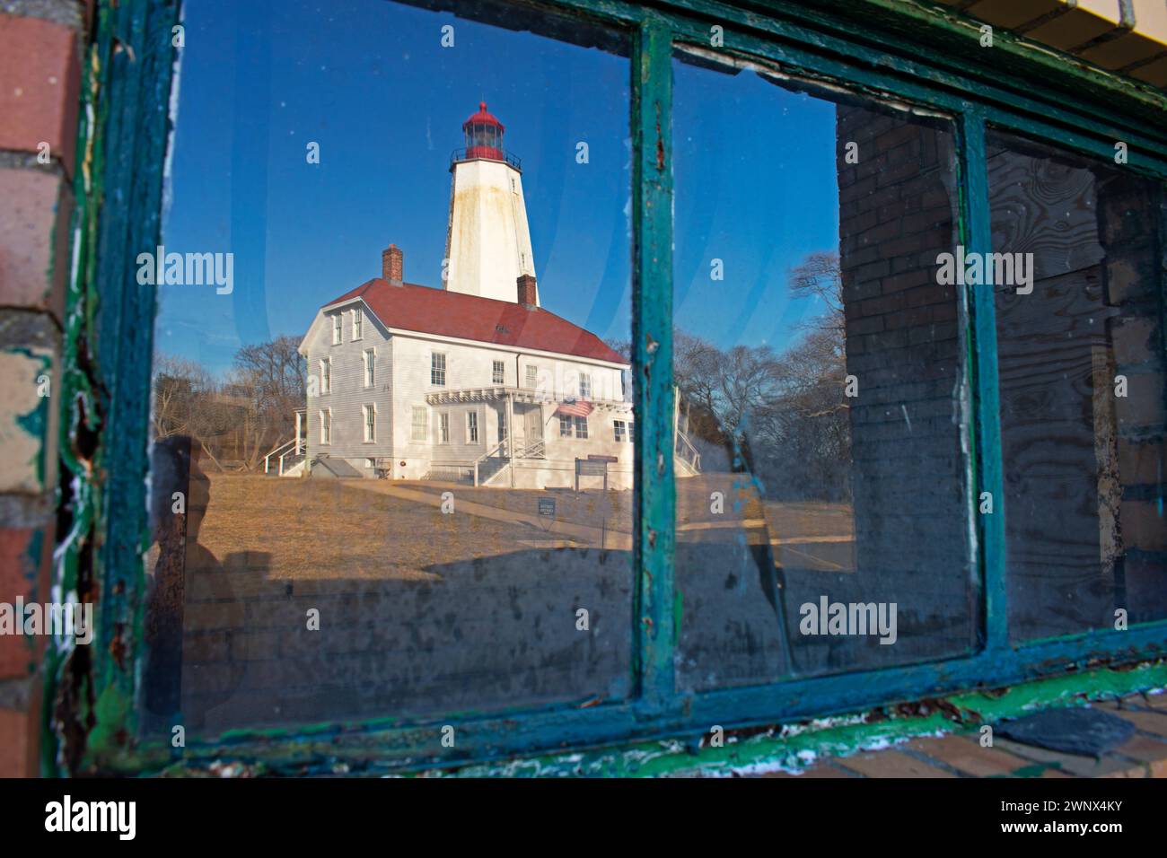 The Sandy Hook Lighthouse reflected on the partially cracked window pane of a Fort Hancock structure -91 Stock Photo