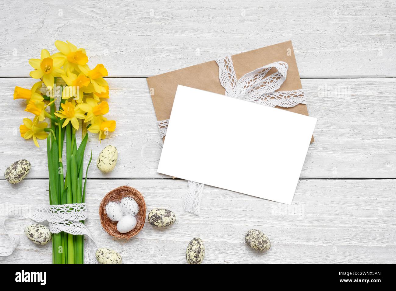 Easter greeting card with spring yellow Narcissus flowers and easter colorful eggs on white wooden background. Flat lay. Mock up. Top view with copy Stock Photo