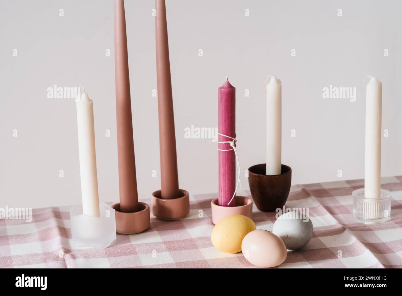 Easter place setting with candles and multi colored eggs, linen tablecloth, white background Stock Photo